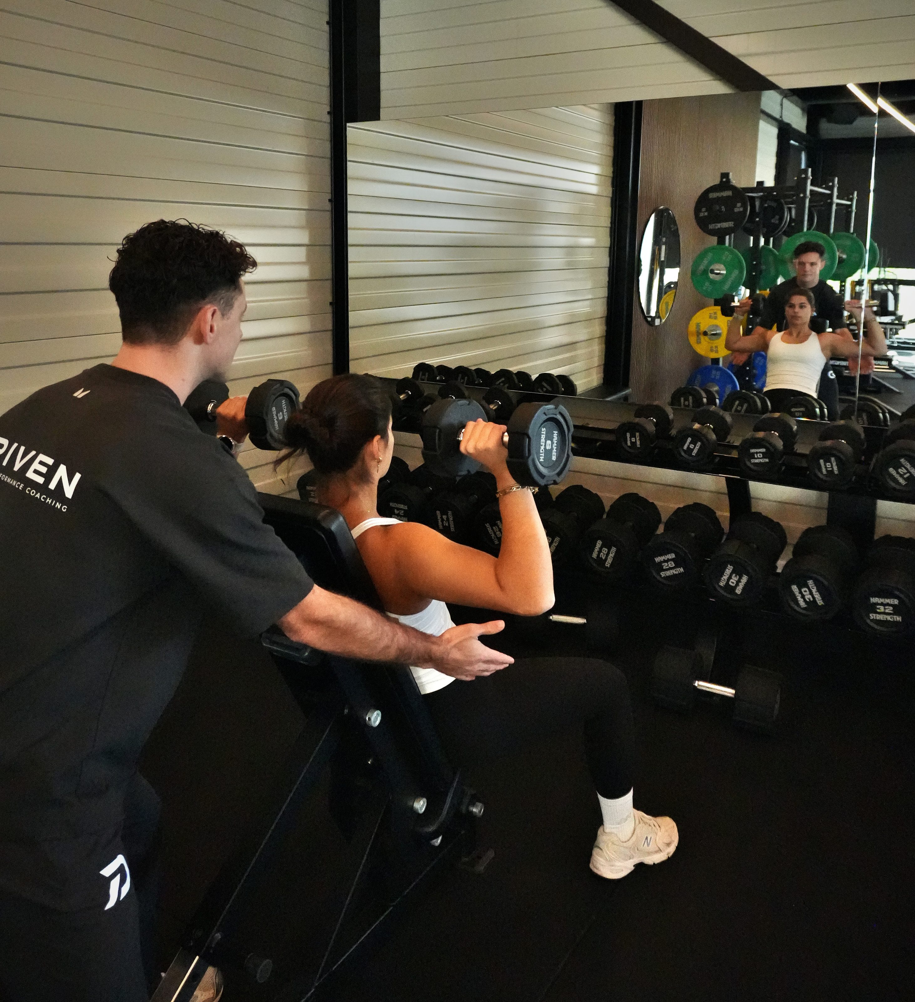 Laurens begeleidt een klant bij een shoulder press met dumbbells