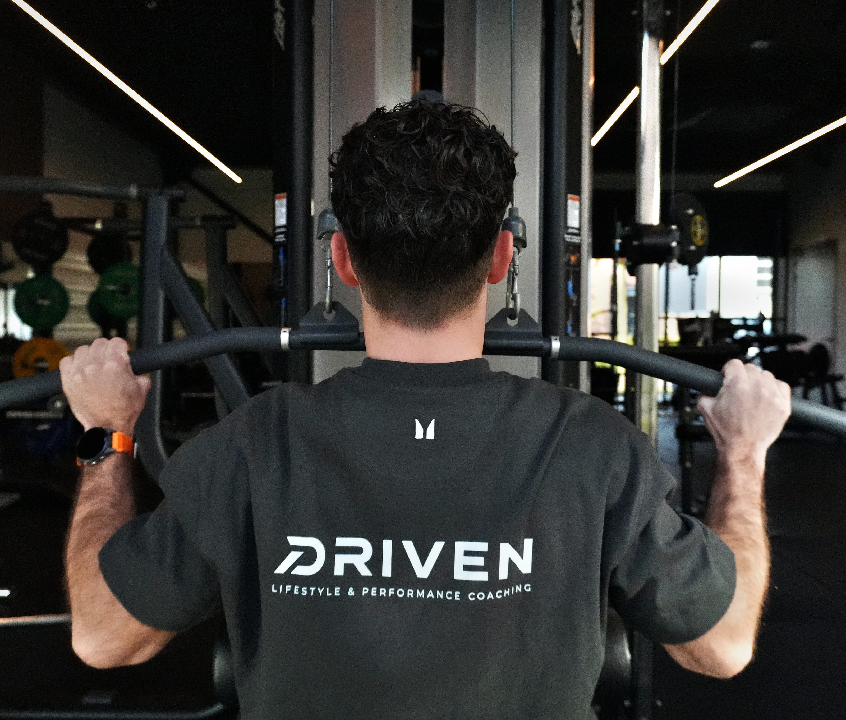 Laurens op de lat pulldown, van achteren, met DRIVEN op zijn shirt
