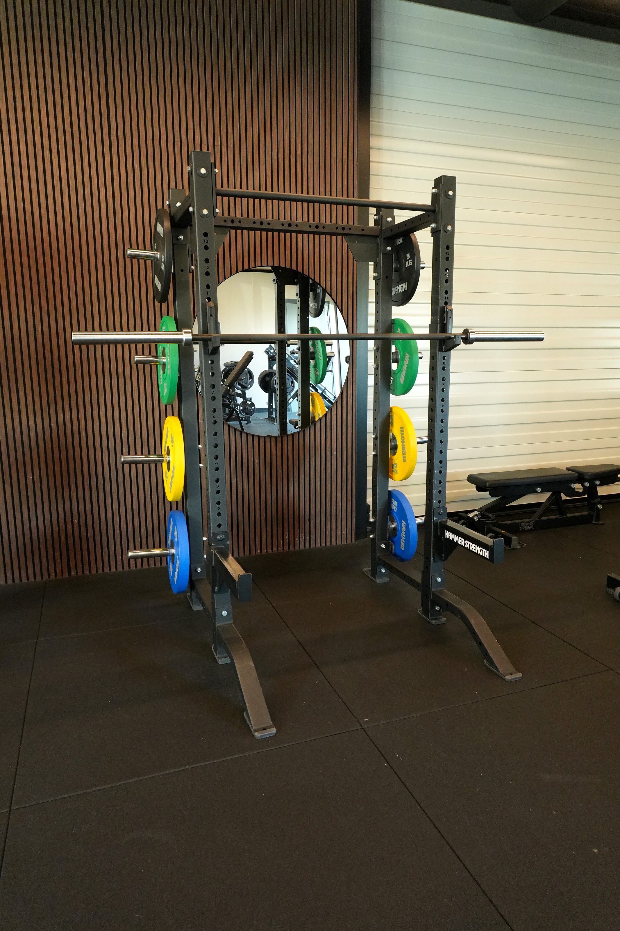 Een squatrek met halterstang voor een houten wand in Fitness4All